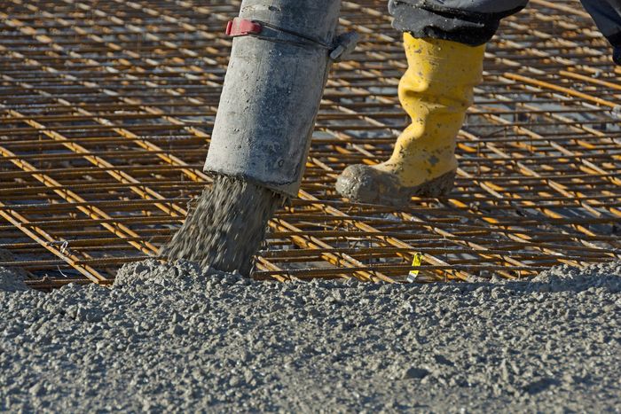 A person wearing yellow boots is pouring concrete on a construction site.
