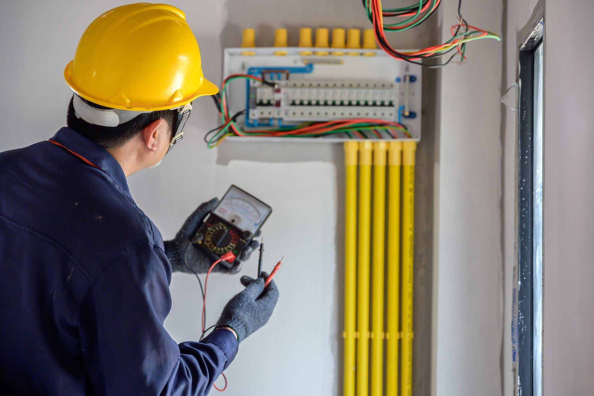 An electrician is using a multimeter to test an electrical box.