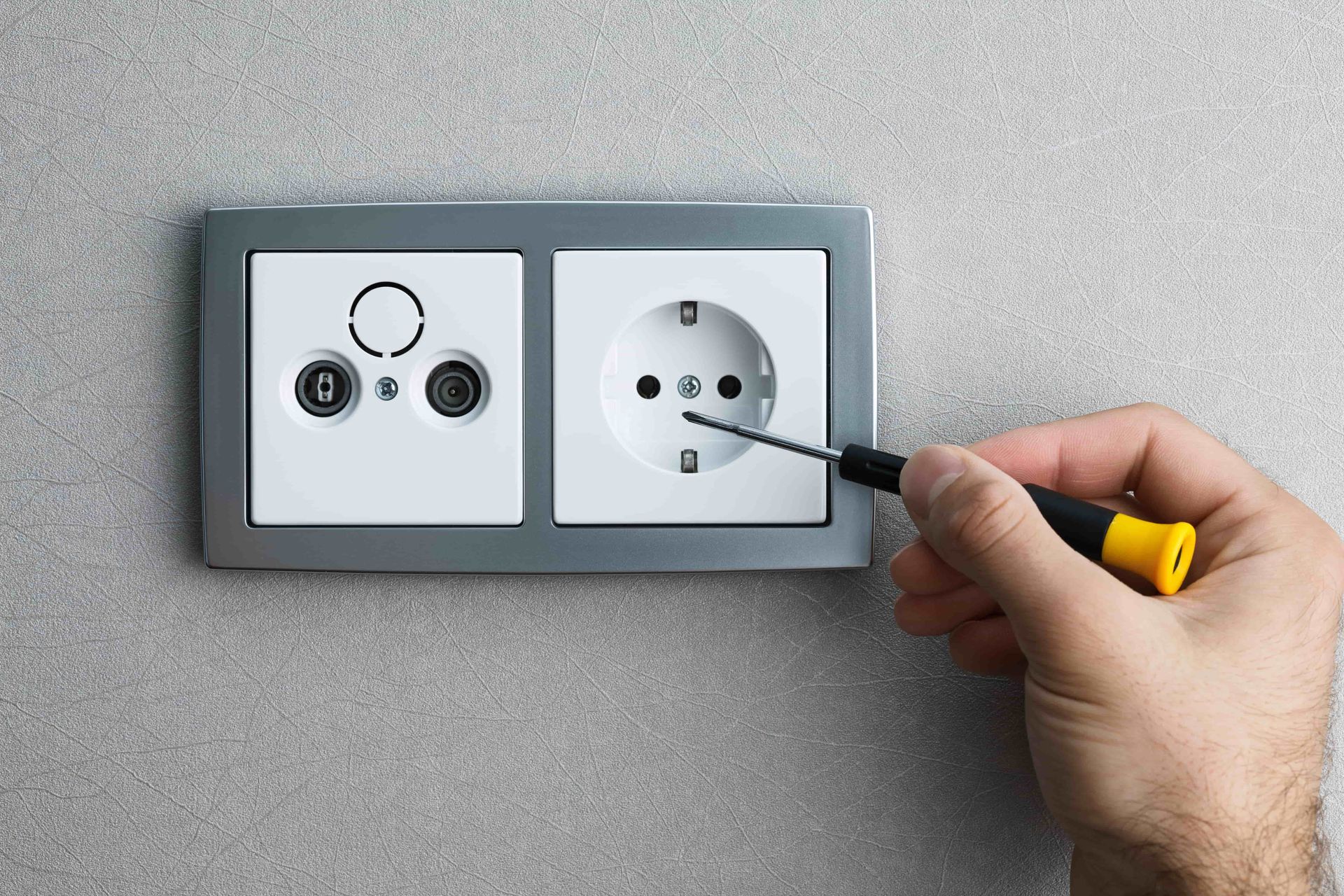 A person is fixing a light switch with a screwdriver.