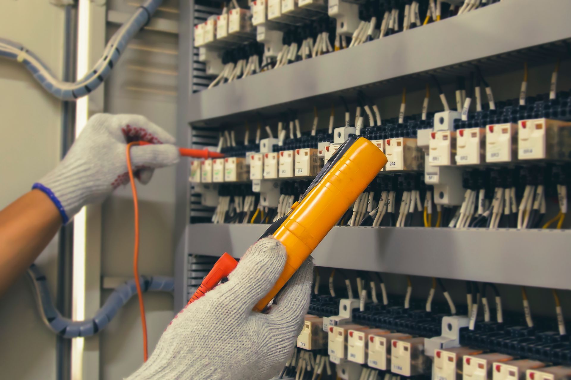 Electrician using a multimeter to test wires in an electrical panel.