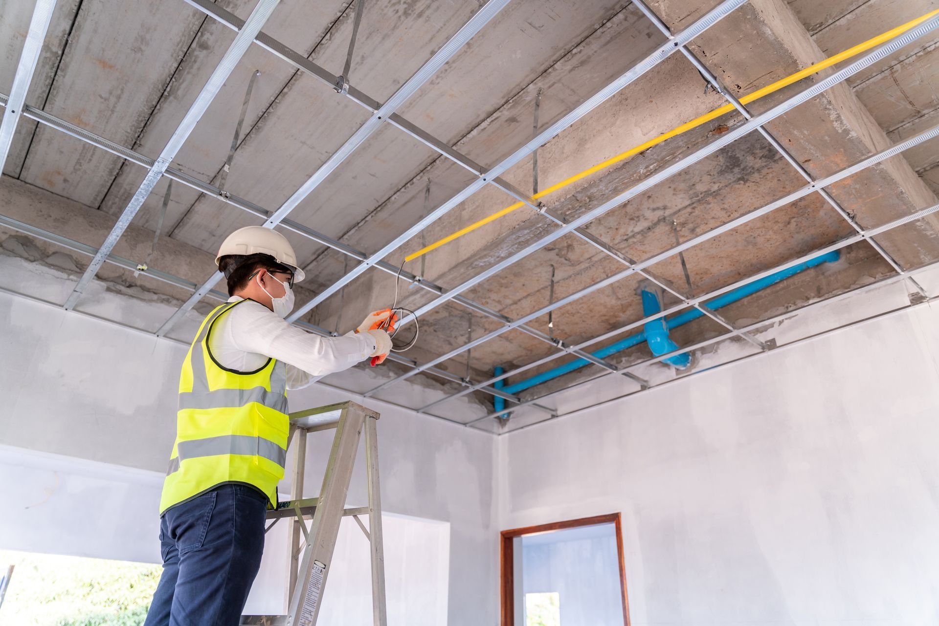 Construction worker in hard hat and vest installs ceiling grid.