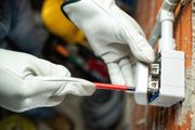 Electrician wearing white gloves using a screwdriver to wire a wall outlet.