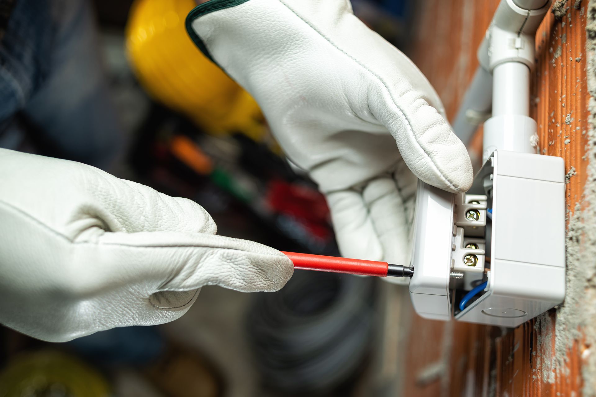 Electrician wearing white gloves using a screwdriver to wire a wall outlet. Electrician wearing white gloves using a screwdriver to wire a wall outlet.