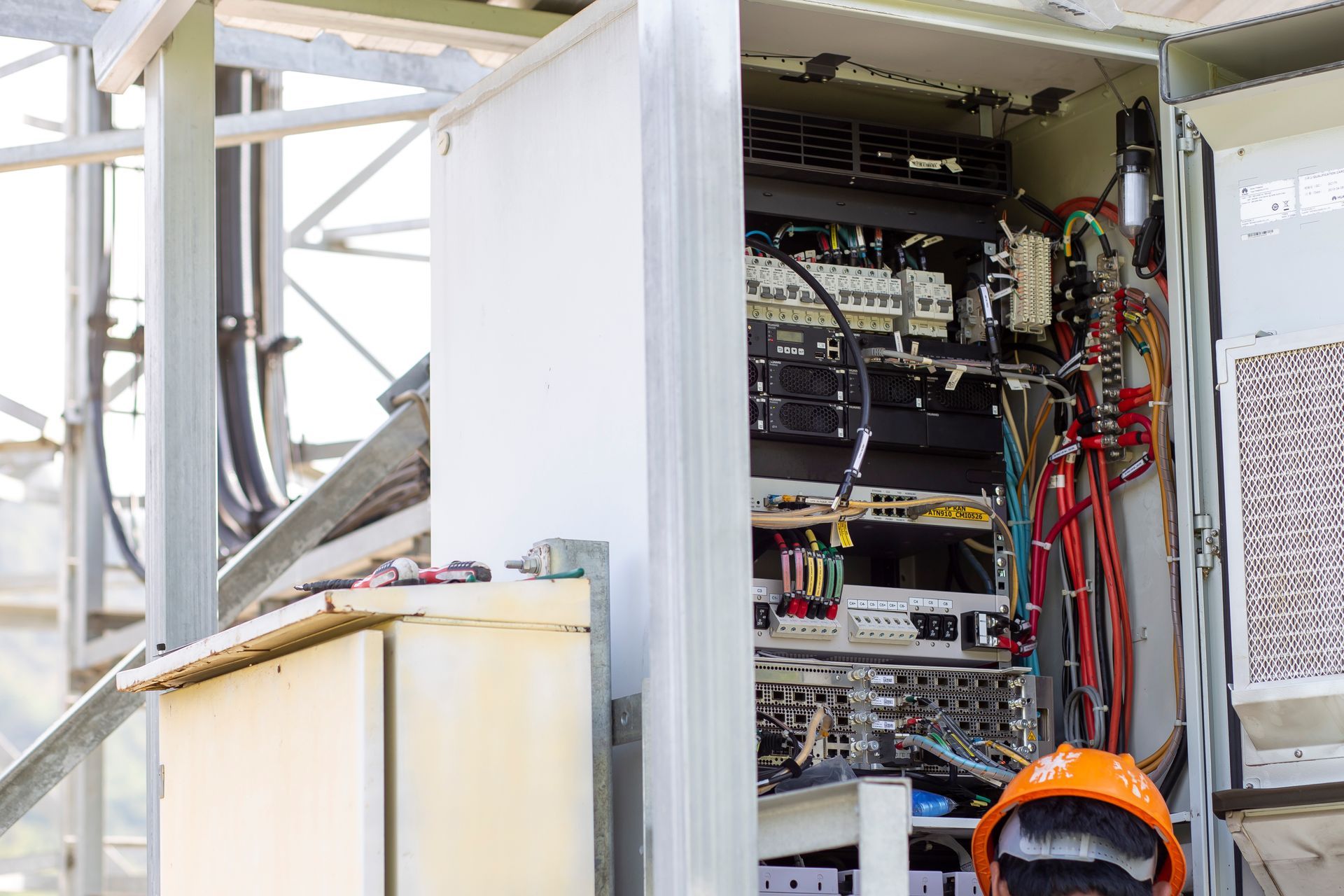 Open electrical cabinet with wires, circuits, and cooling unit on a metal structure.