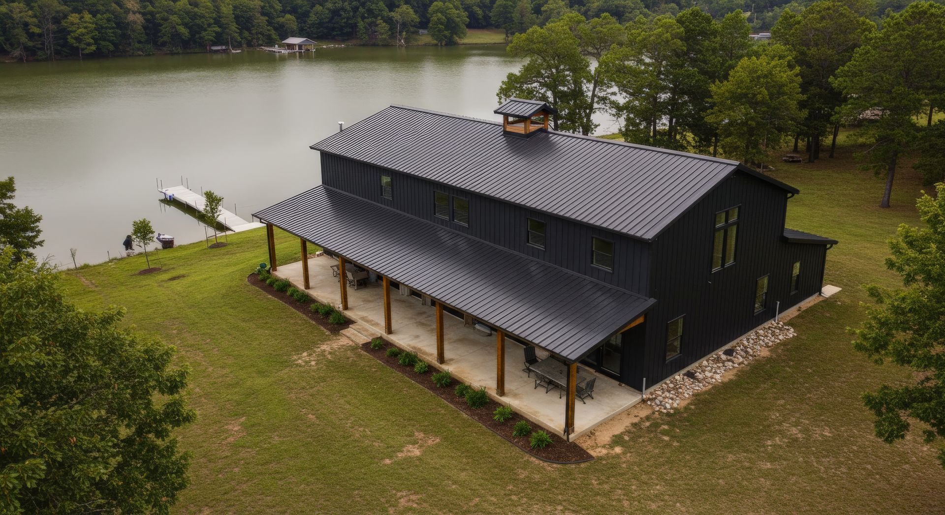 An aerial view of a large black barn next to a lake.