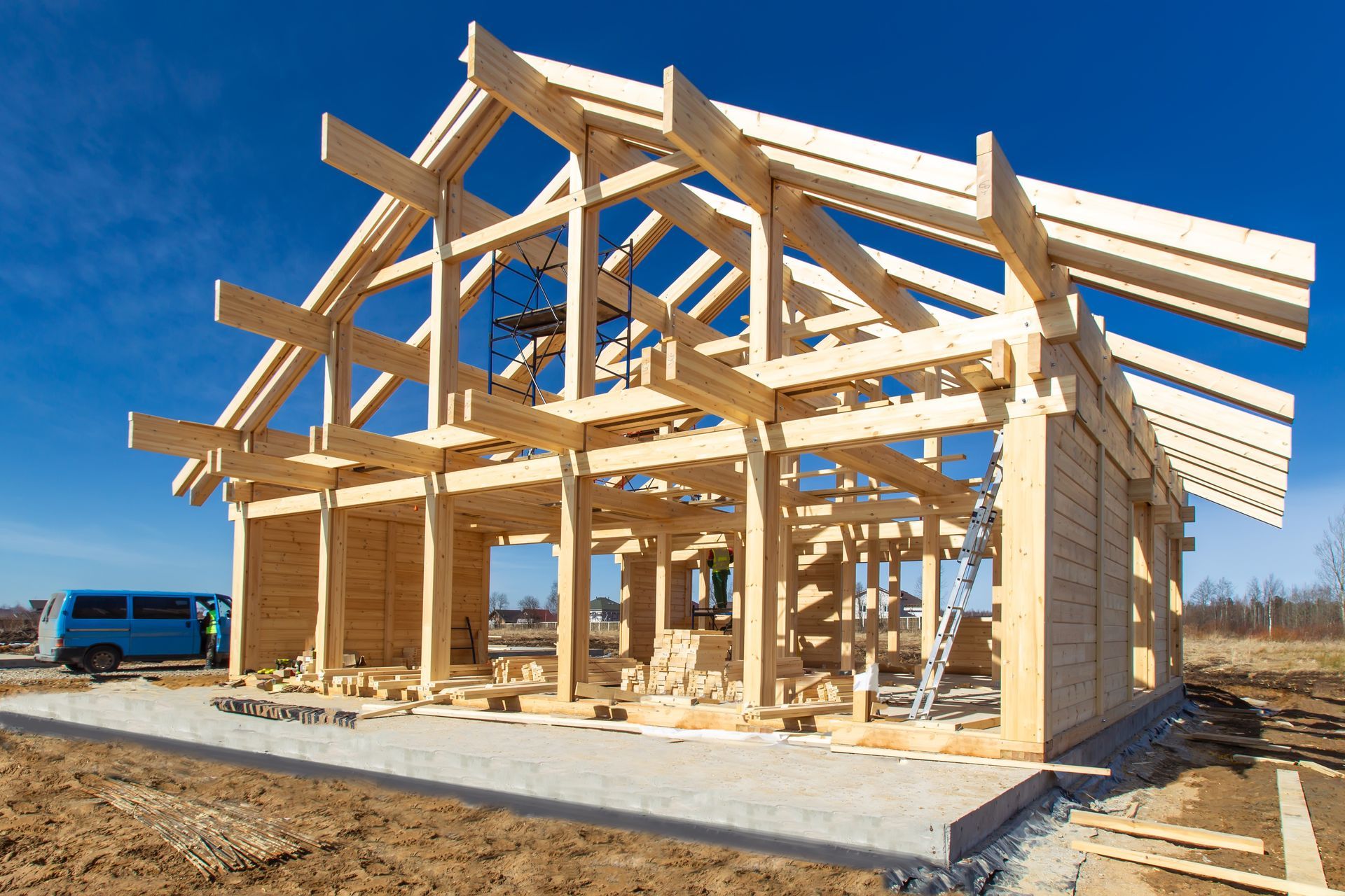 A blue van is parked in front of a wooden house under construction.