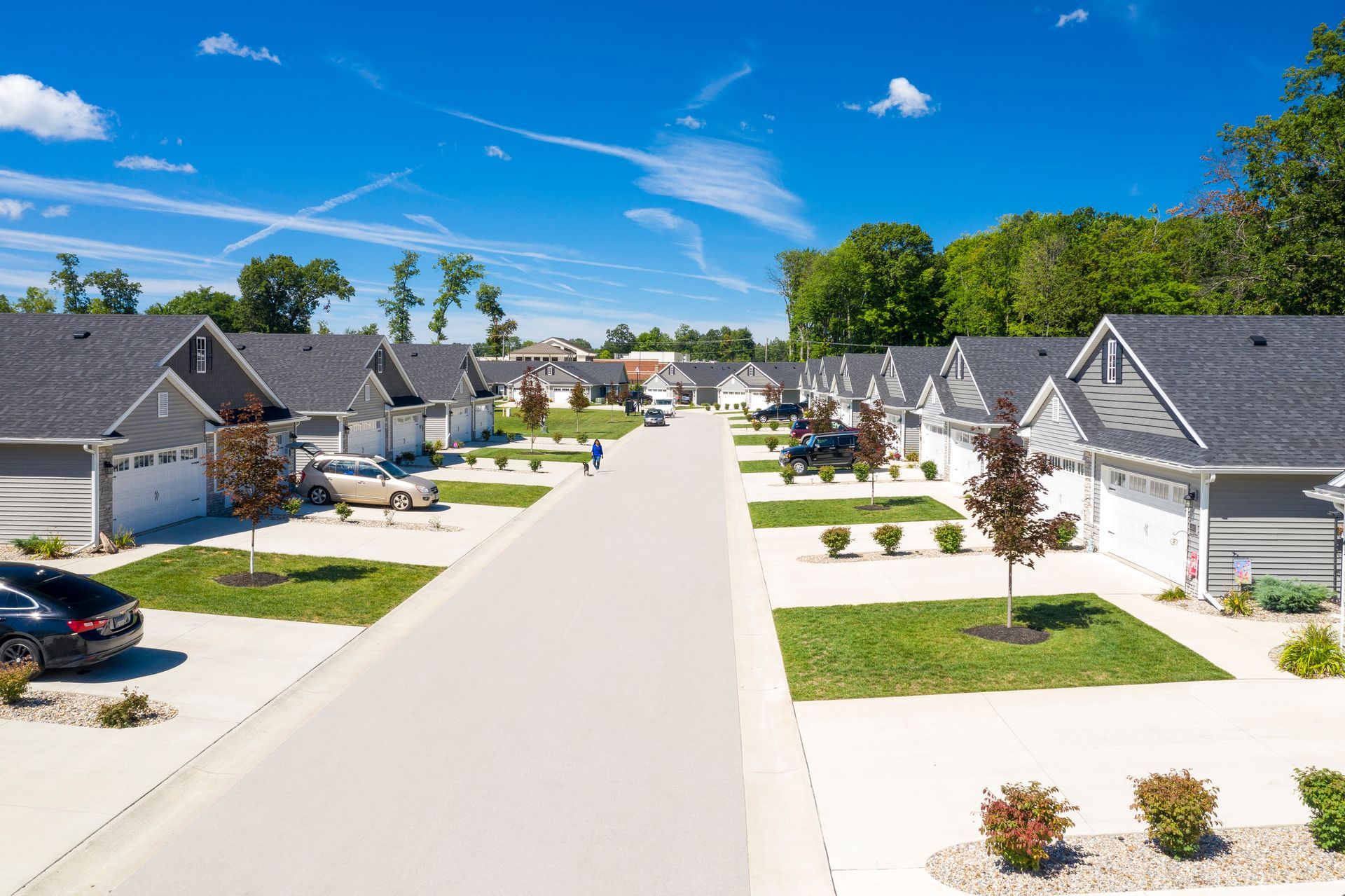 A residential street with gray houses, green lawns, and a blue sky.