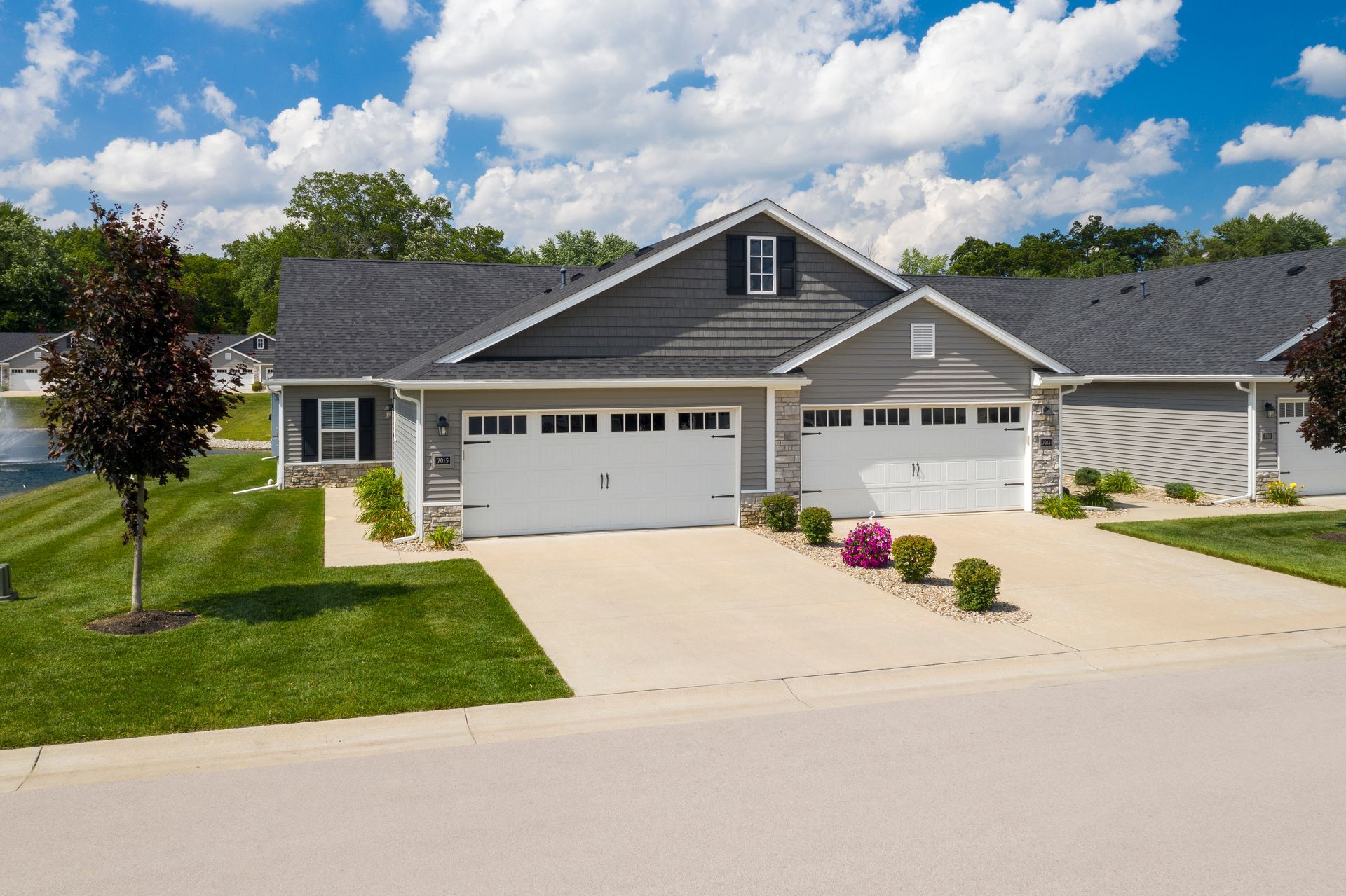 Gray and white townhomes with white garage doors and manicured lawns under a blue sky.