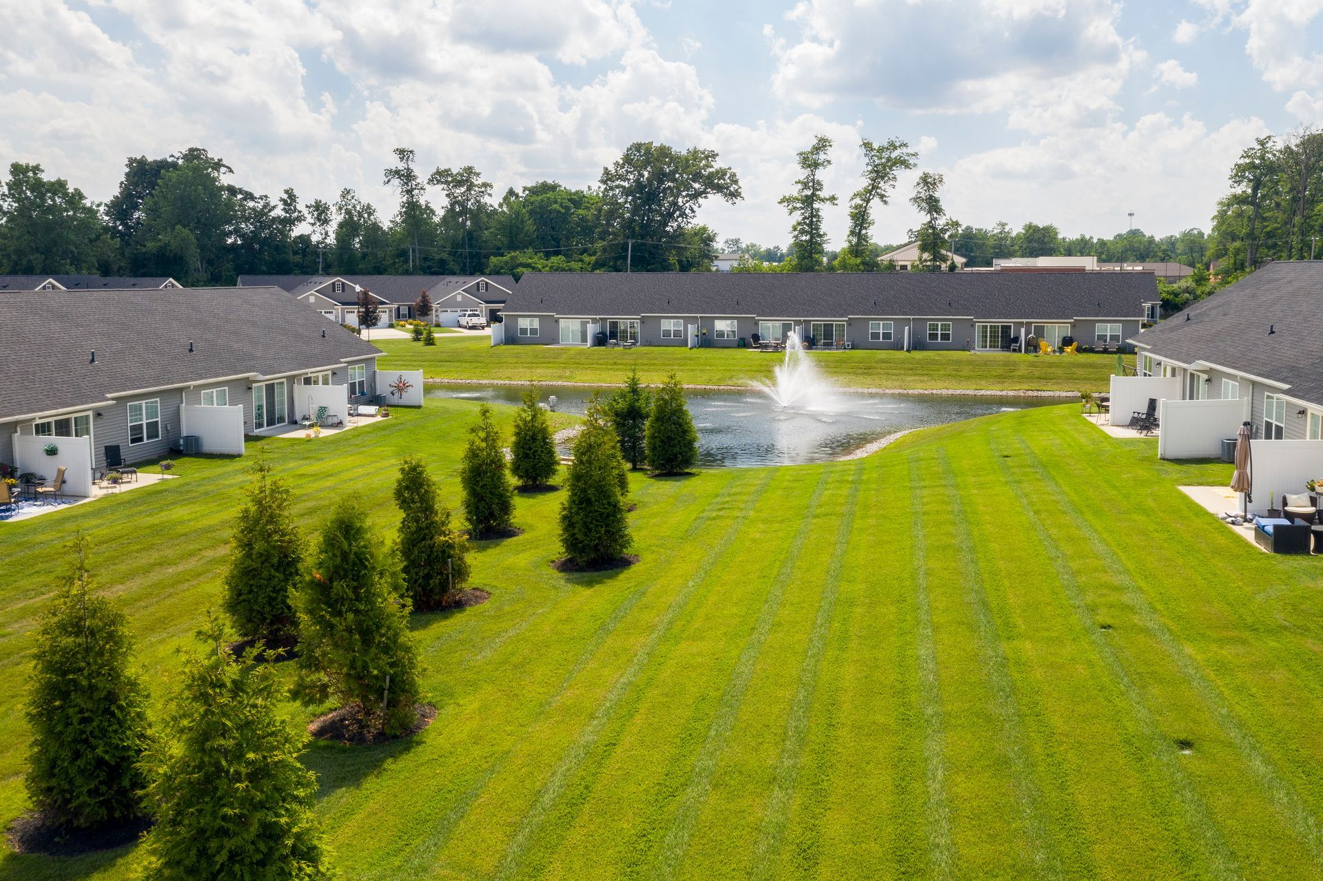 Aerial view of a suburban community with townhouses, a pond with a fountain, and green lawns.