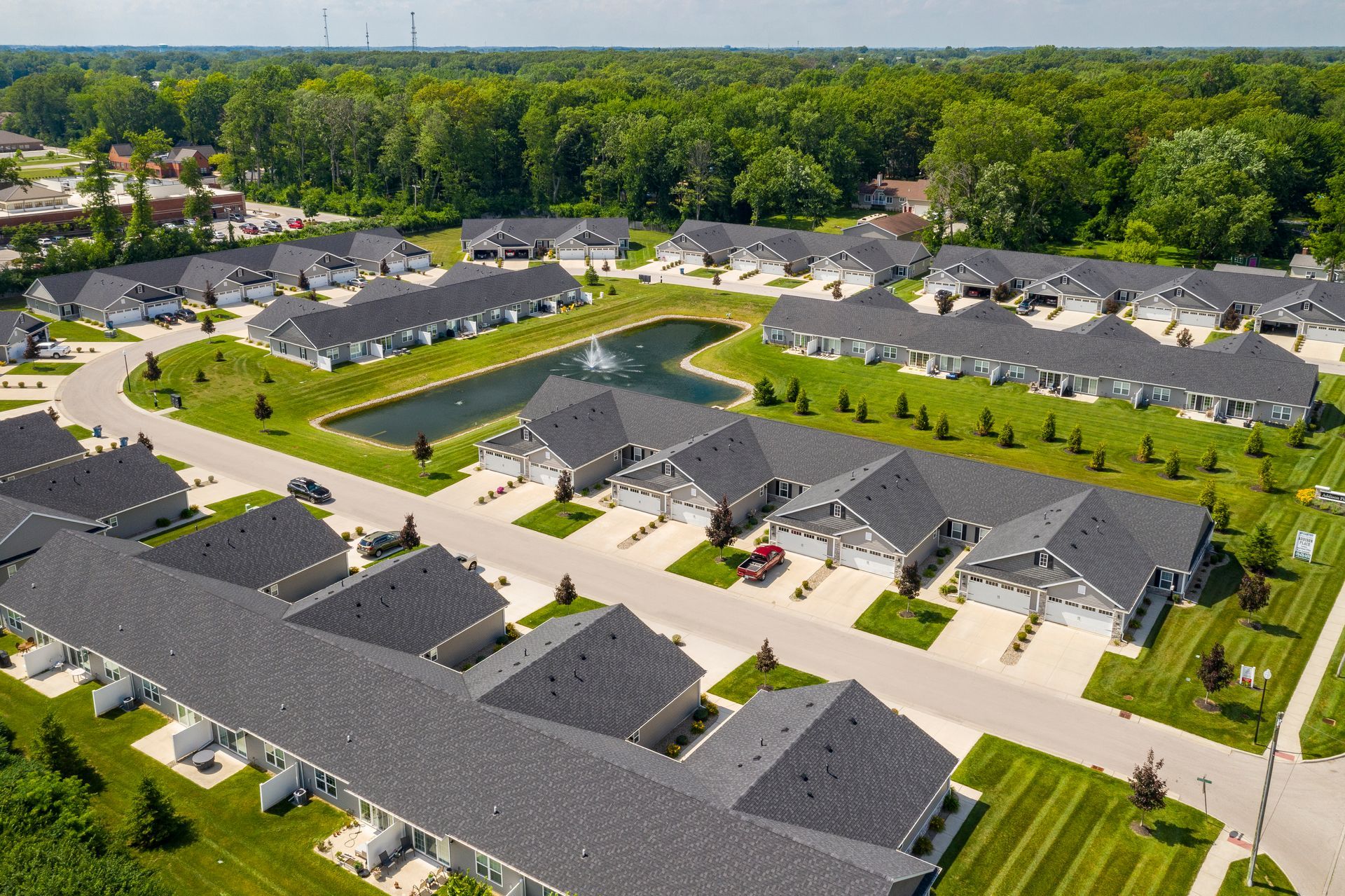 Aerial view of a suburban residential community with rows of houses, a pond, and green lawns.