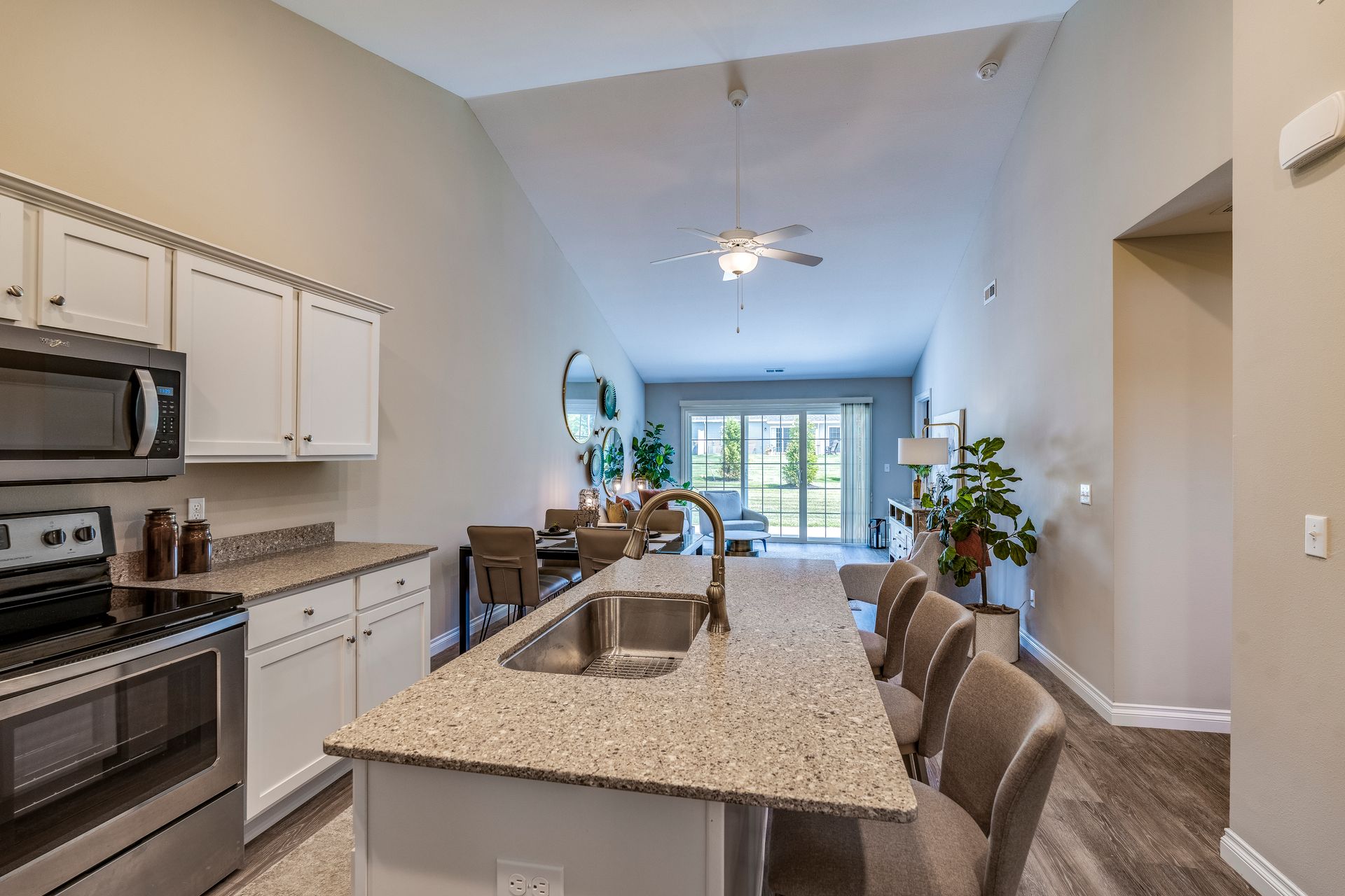 Kitchen with island and stainless steel appliances, opening to living area with high ceilings and natural light.