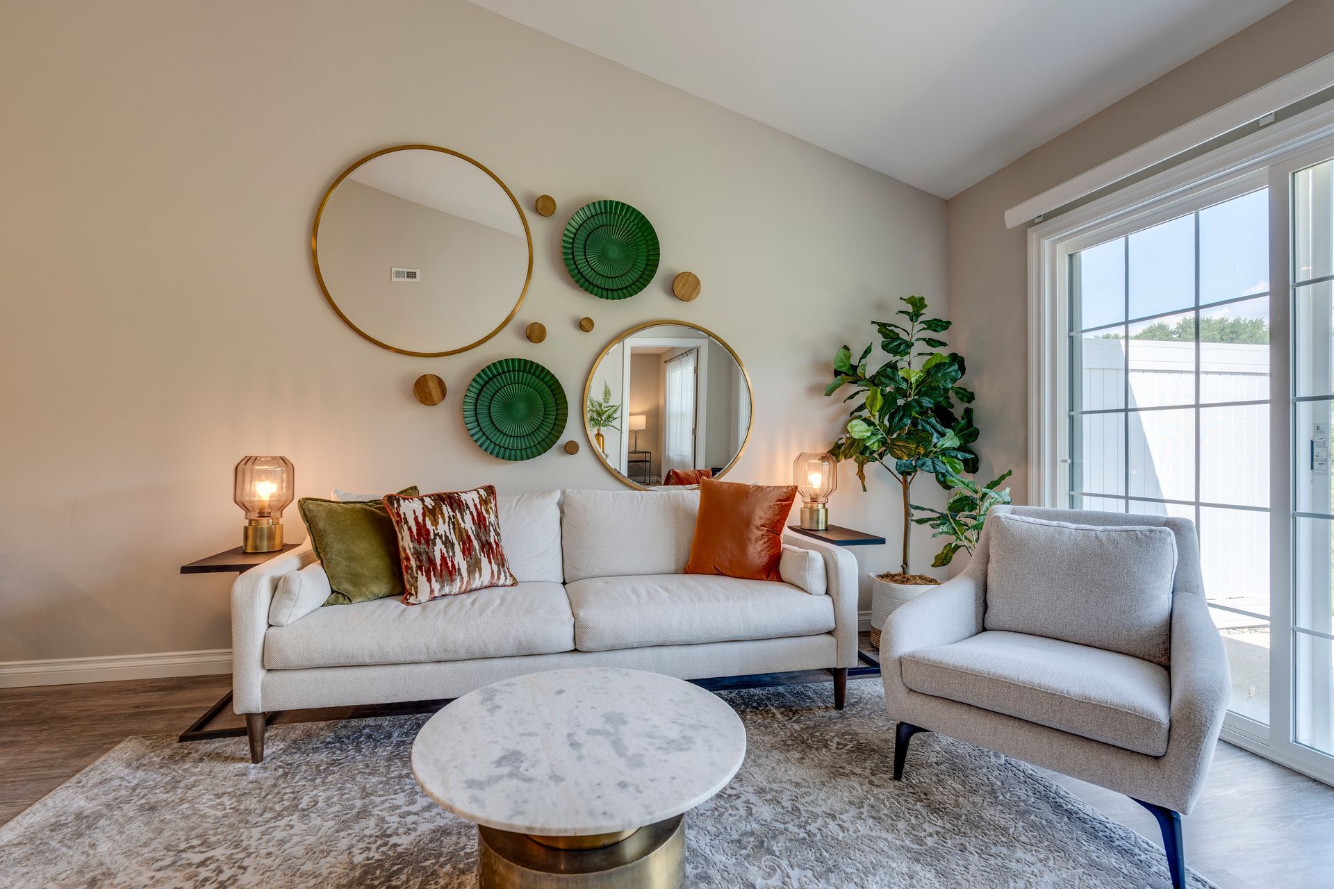 Living room with sofa, armchair, coffee table, mirrors, and sliding glass door.
