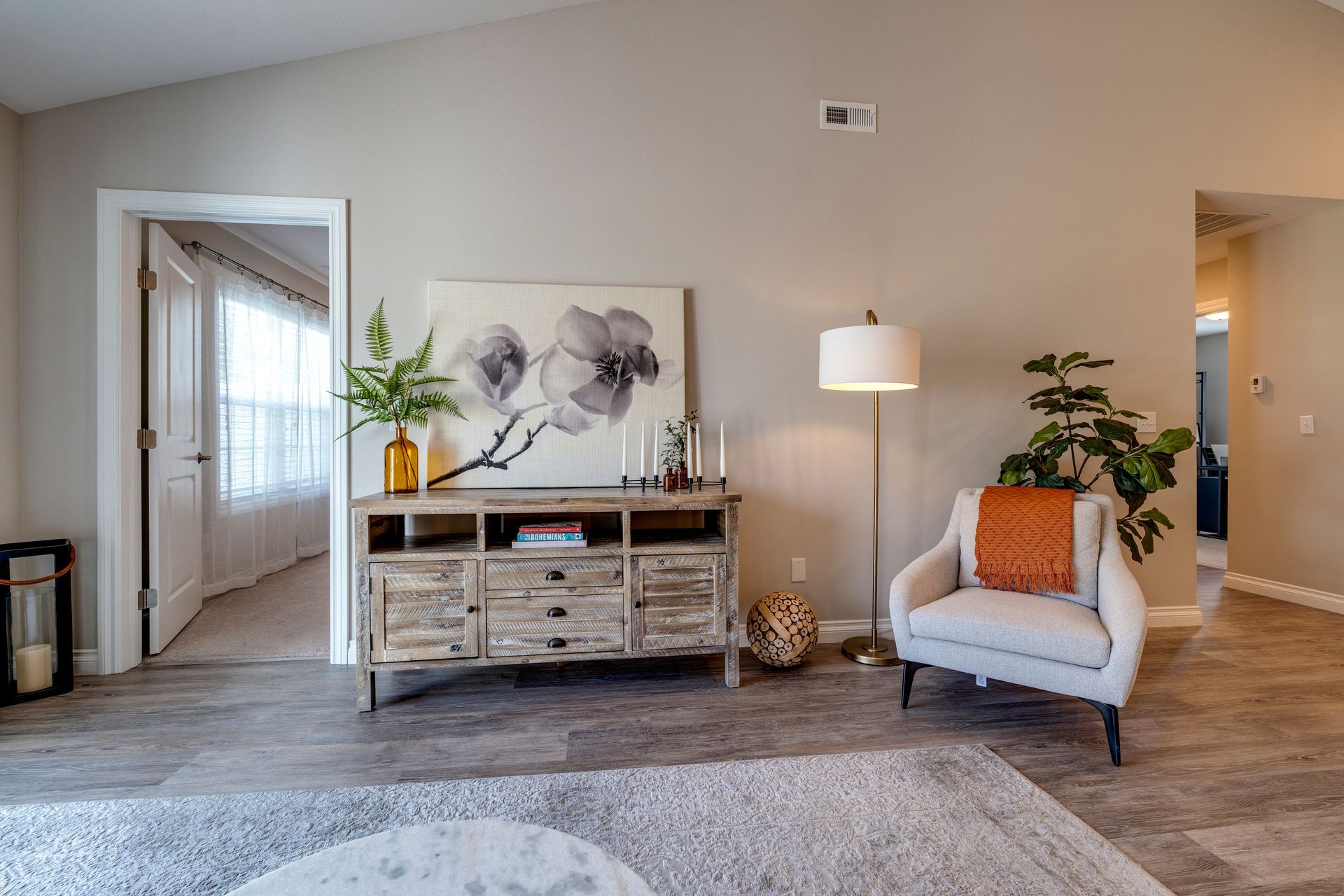 Living room with neutral tones, rustic cabinet, white armchair, and large floral painting.