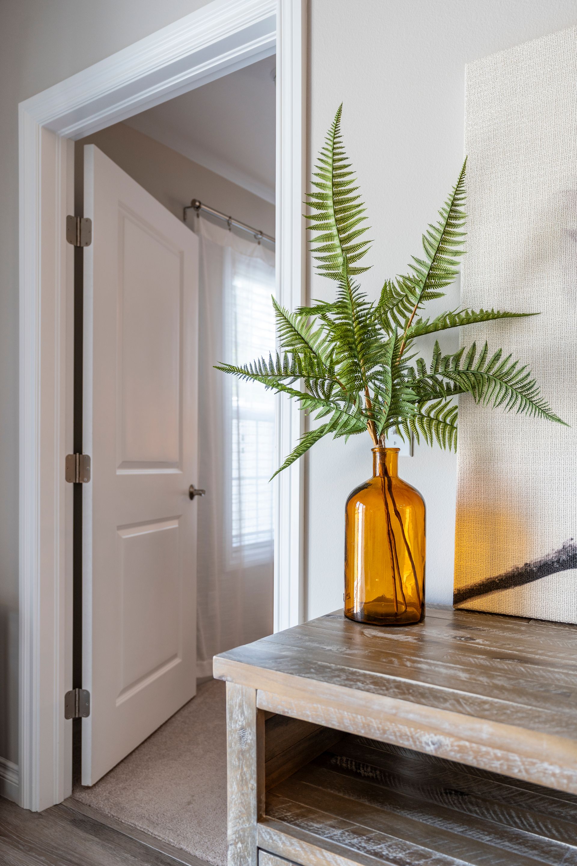 Wooden cabinet with an amber vase holding fern branches next to an open door.