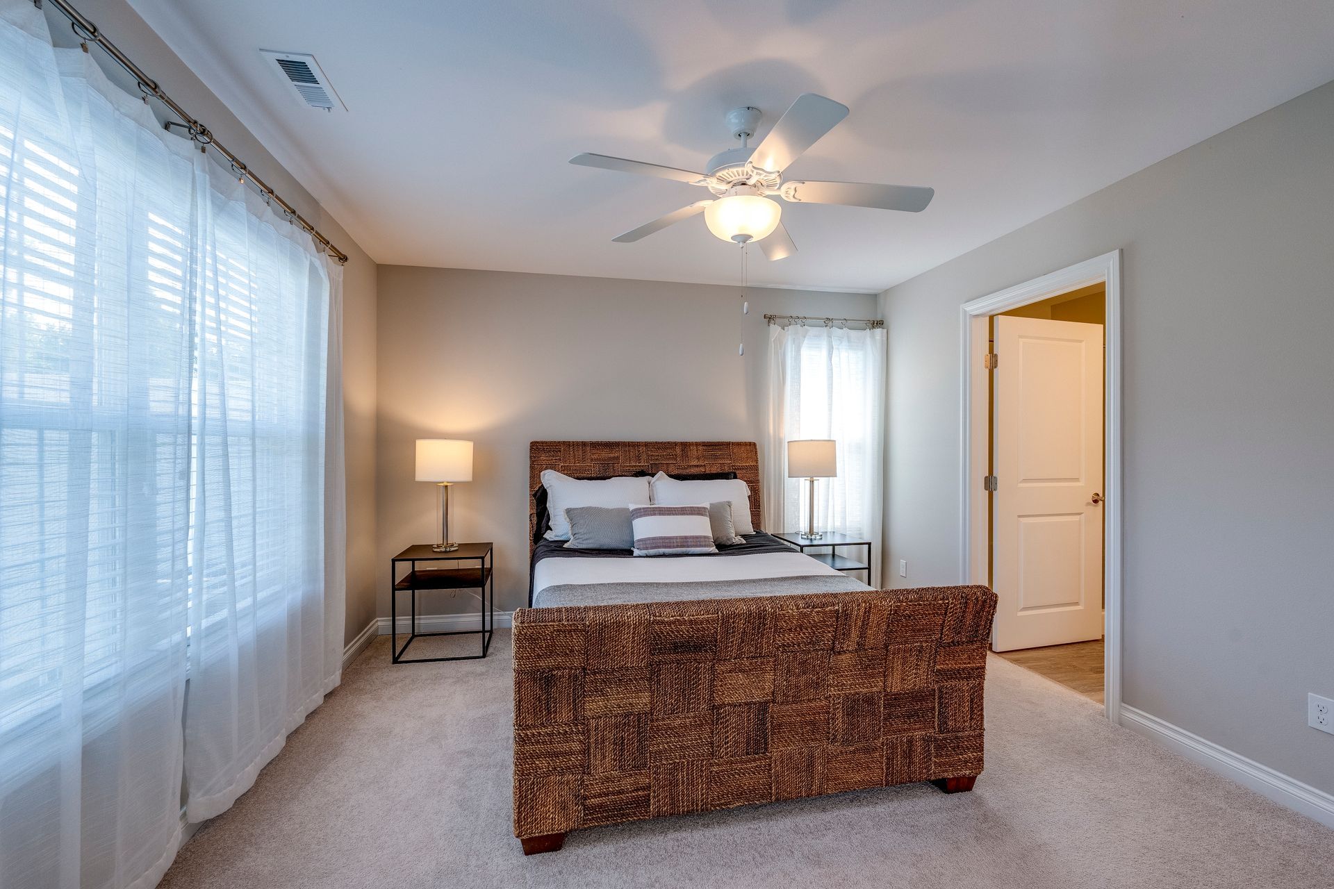 Bedroom with bed, nightstands, windows with sheer curtains, ceiling fan.