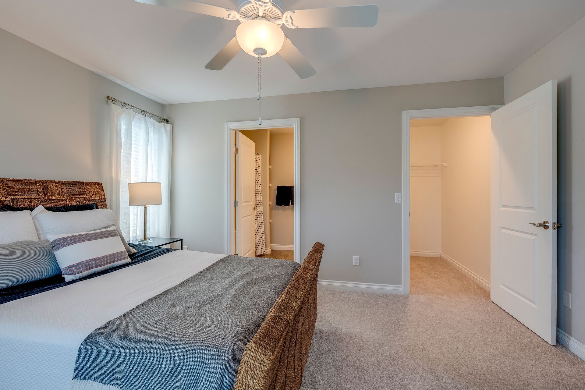 Bedroom with bed, closet, and bathroom. Neutral walls and flooring, ceiling fan.
