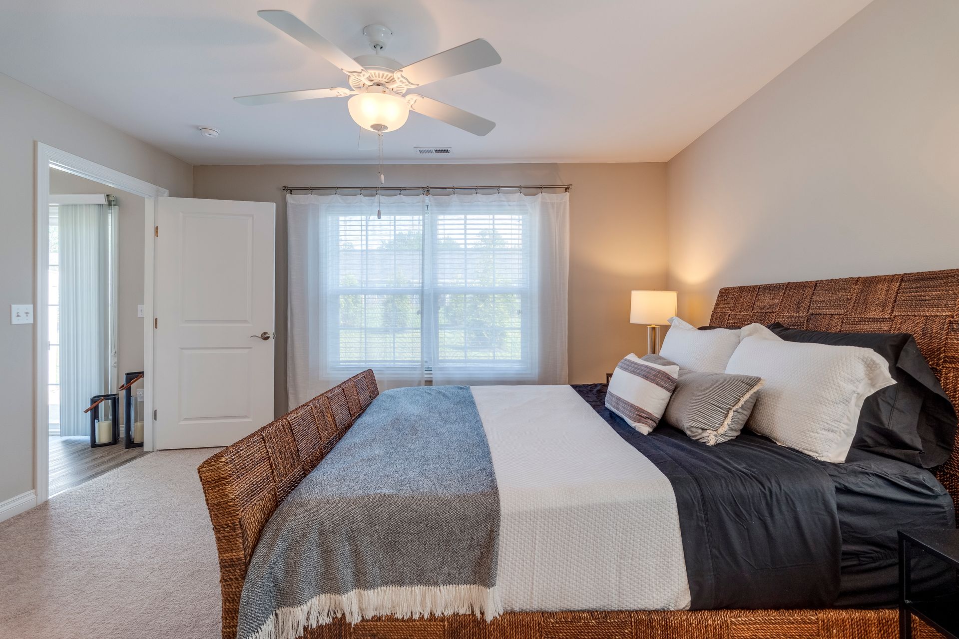 Bedroom with a large bed, window with sheer curtains, door to a balcony. Beige walls, ceiling fan.