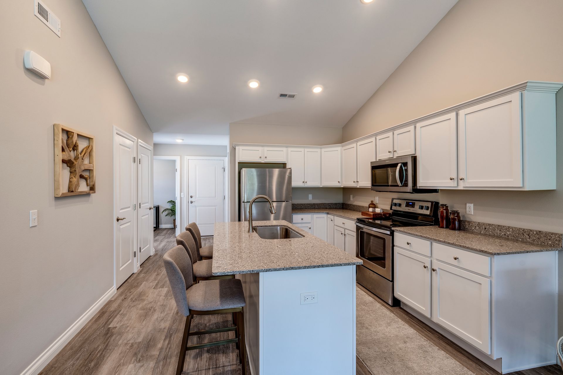 Kitchen with white cabinets, stainless steel appliances, and island with bar stools.