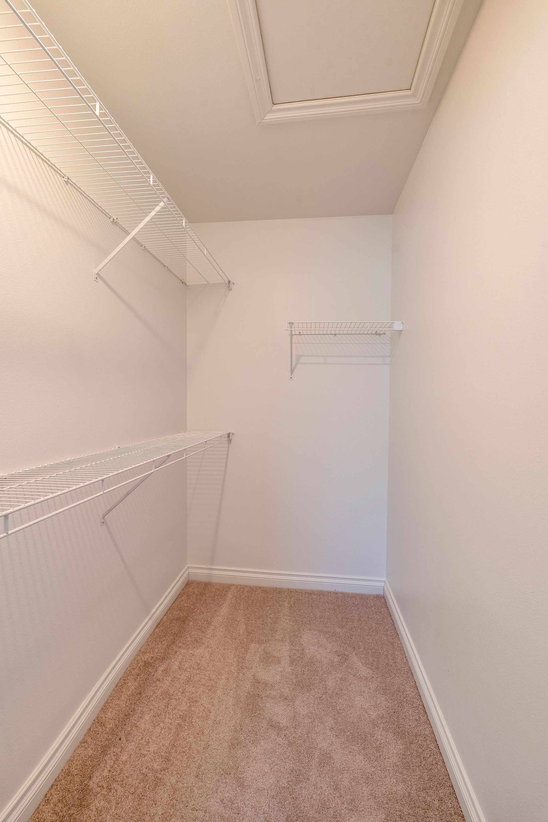 Empty walk-in closet with wire shelves and beige carpet. White walls and ceiling.