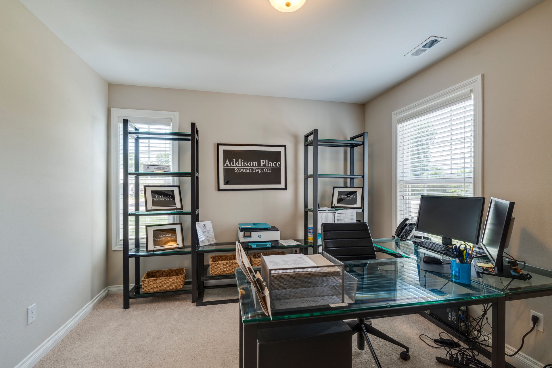Home office with glass desk, black shelves, computer, and window.