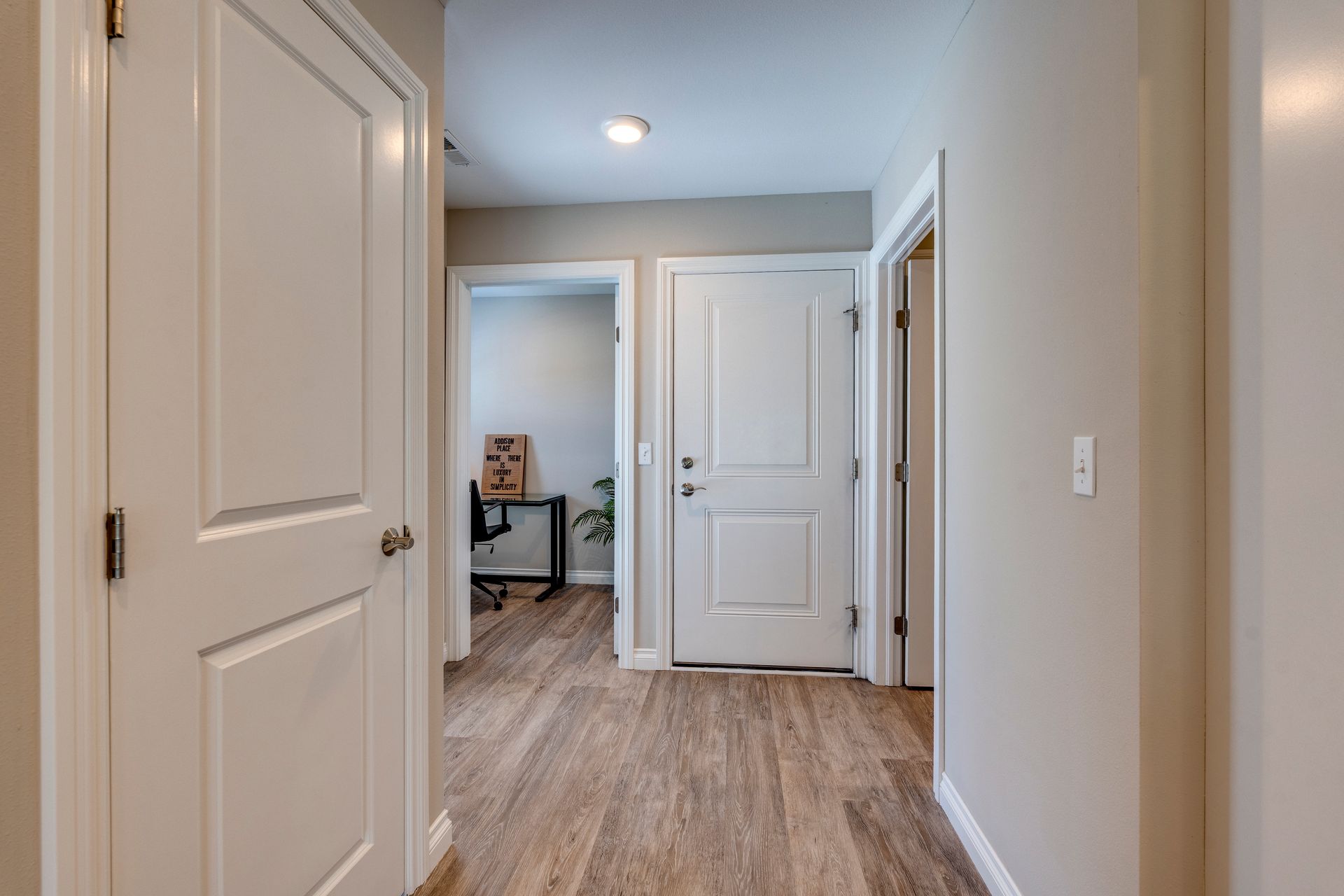 Hallway with light wood floors, white doors, and light gray walls.