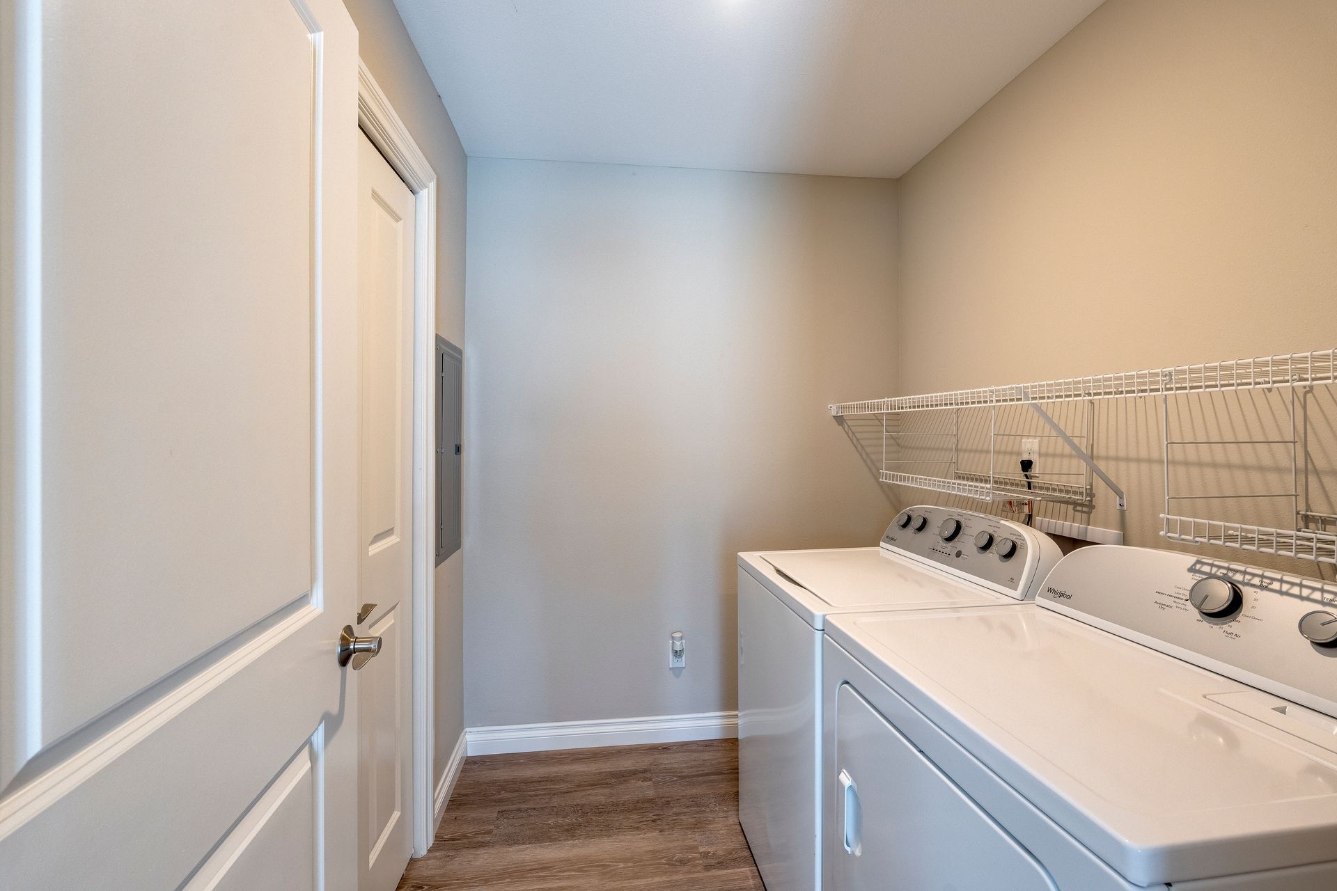 Laundry room with a washing machine, dryer, and shelves. A door is to the left.