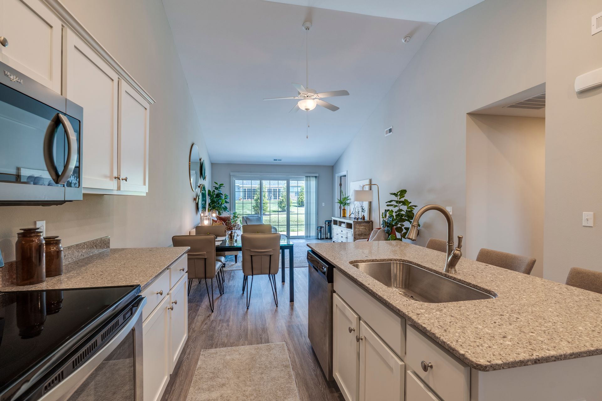 Kitchen with light cabinets, stainless steel appliances, and a view into the living area with a dining table and sliding glass doors.