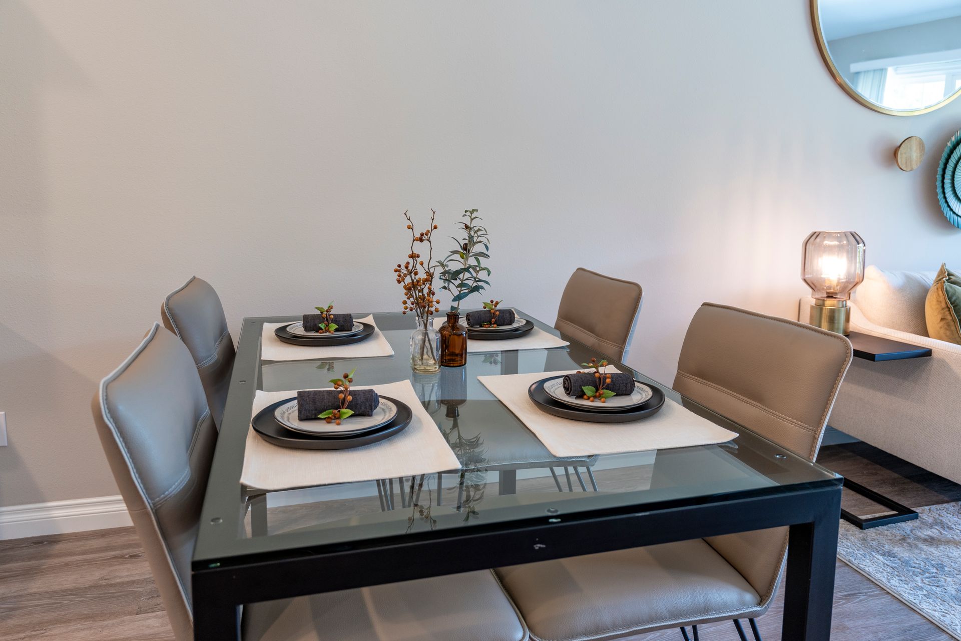 Dining table set for four, with plates, centerpieces, and beige chairs in a brightly lit room.