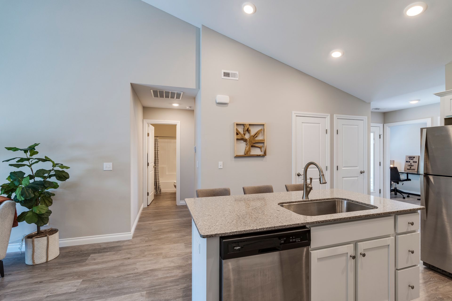 Kitchen with island, stainless steel appliances, and adjacent hallway. Gray walls, light cabinets.