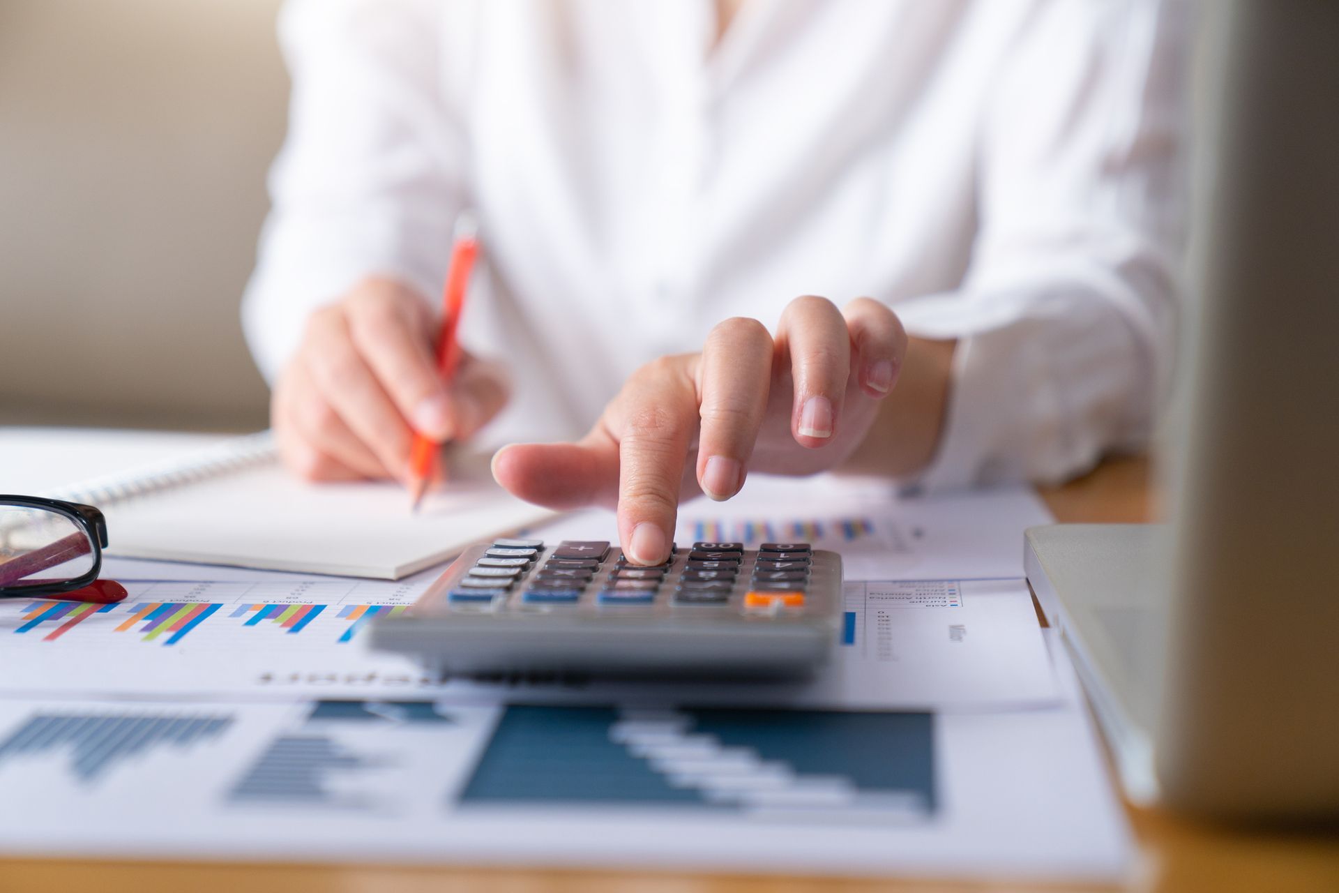 A woman is using a calculator and writing on a piece of paper.