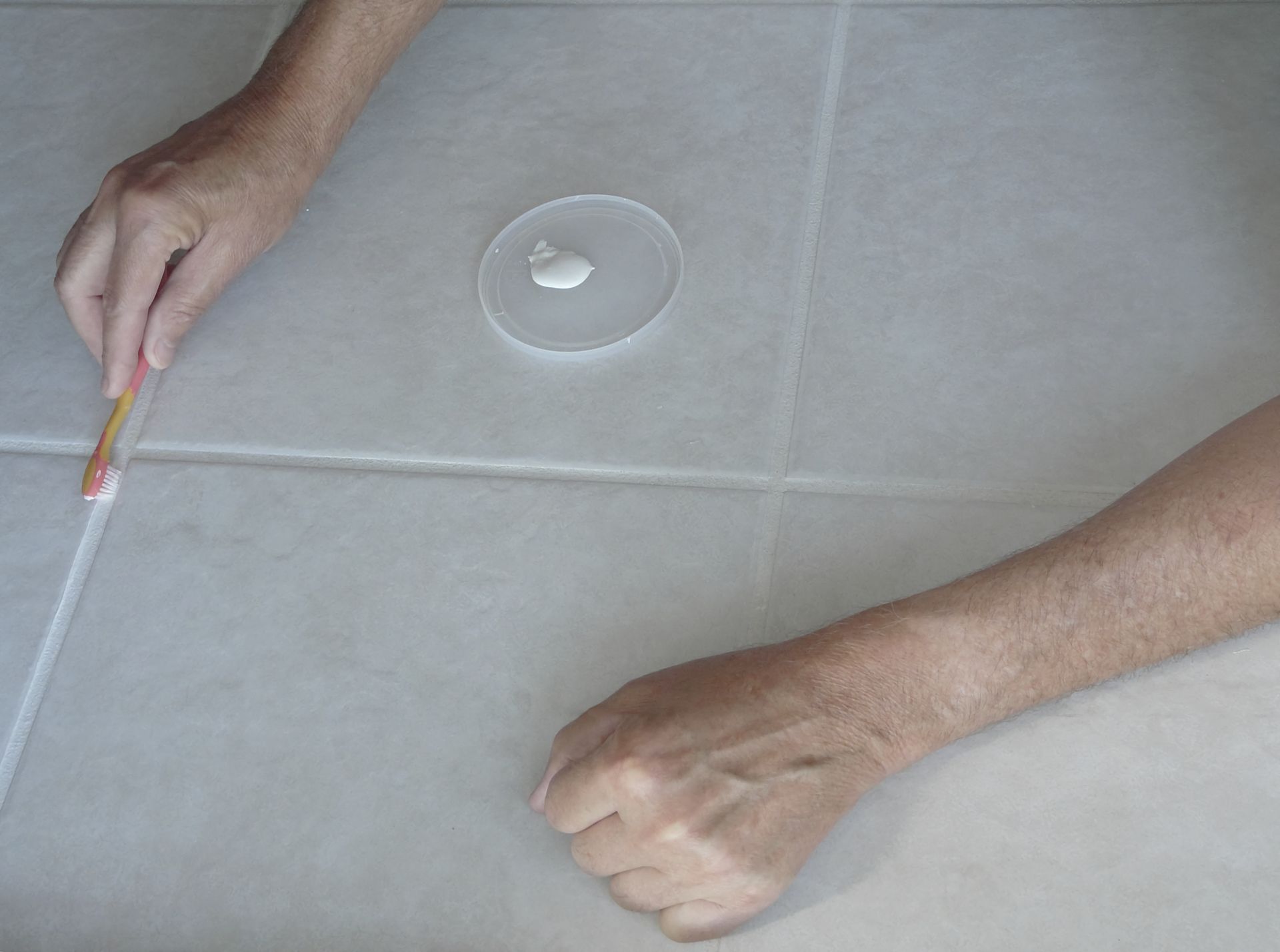Hands applying grout recolor treatment on the bathroom tile floor.
