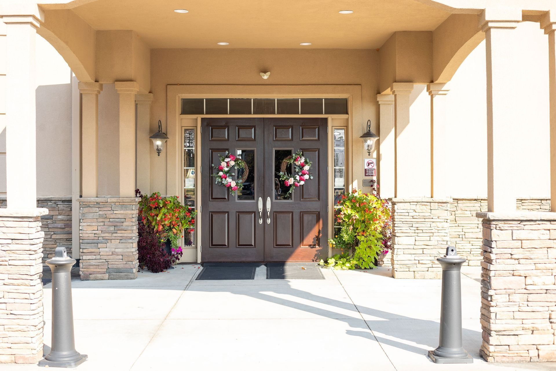 Exterior of building with double doors, wreaths, and flower displays. Beige facade, columns.