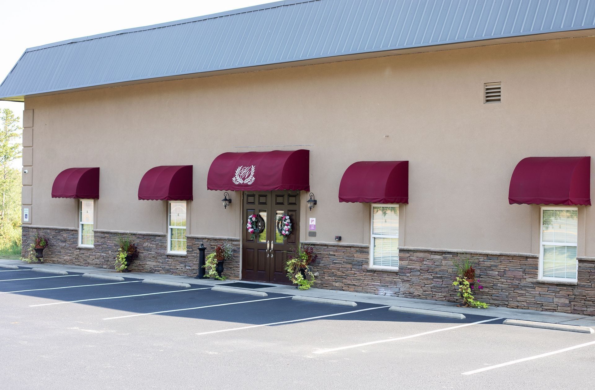 Tan building with burgundy awnings over windows, a black door, and a parking lot.