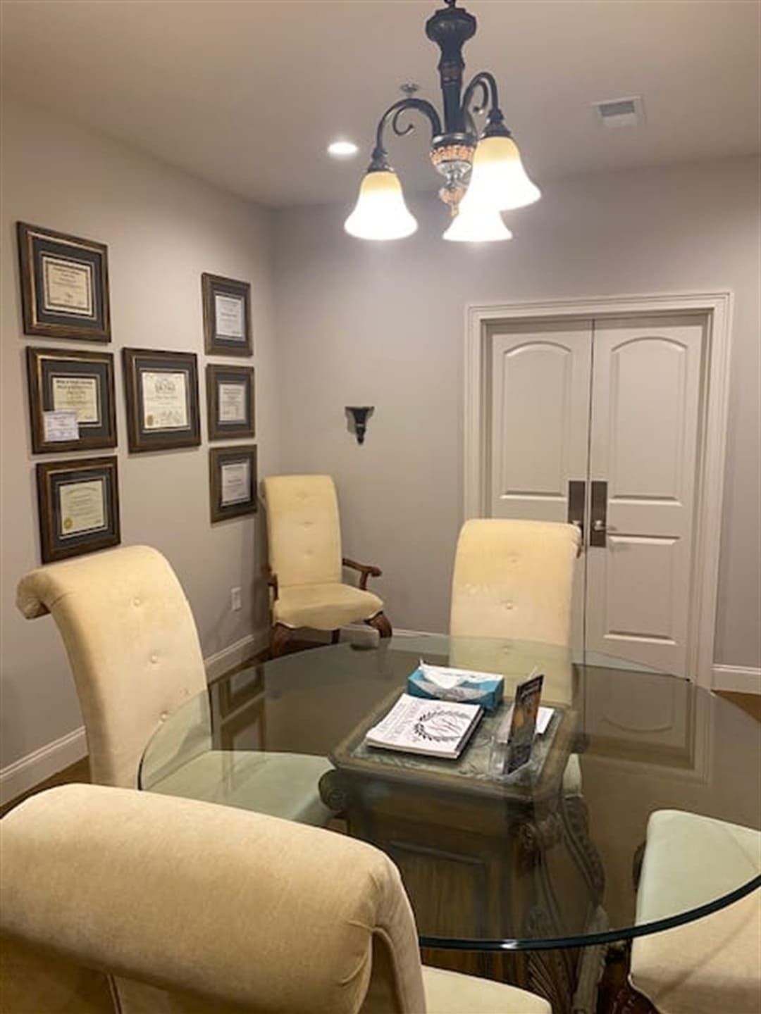 An office meeting room with a glass table, chairs, and framed certificates on the wall.