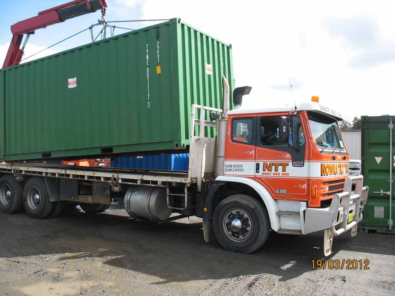 flatbed truck being loaded with green storage container
