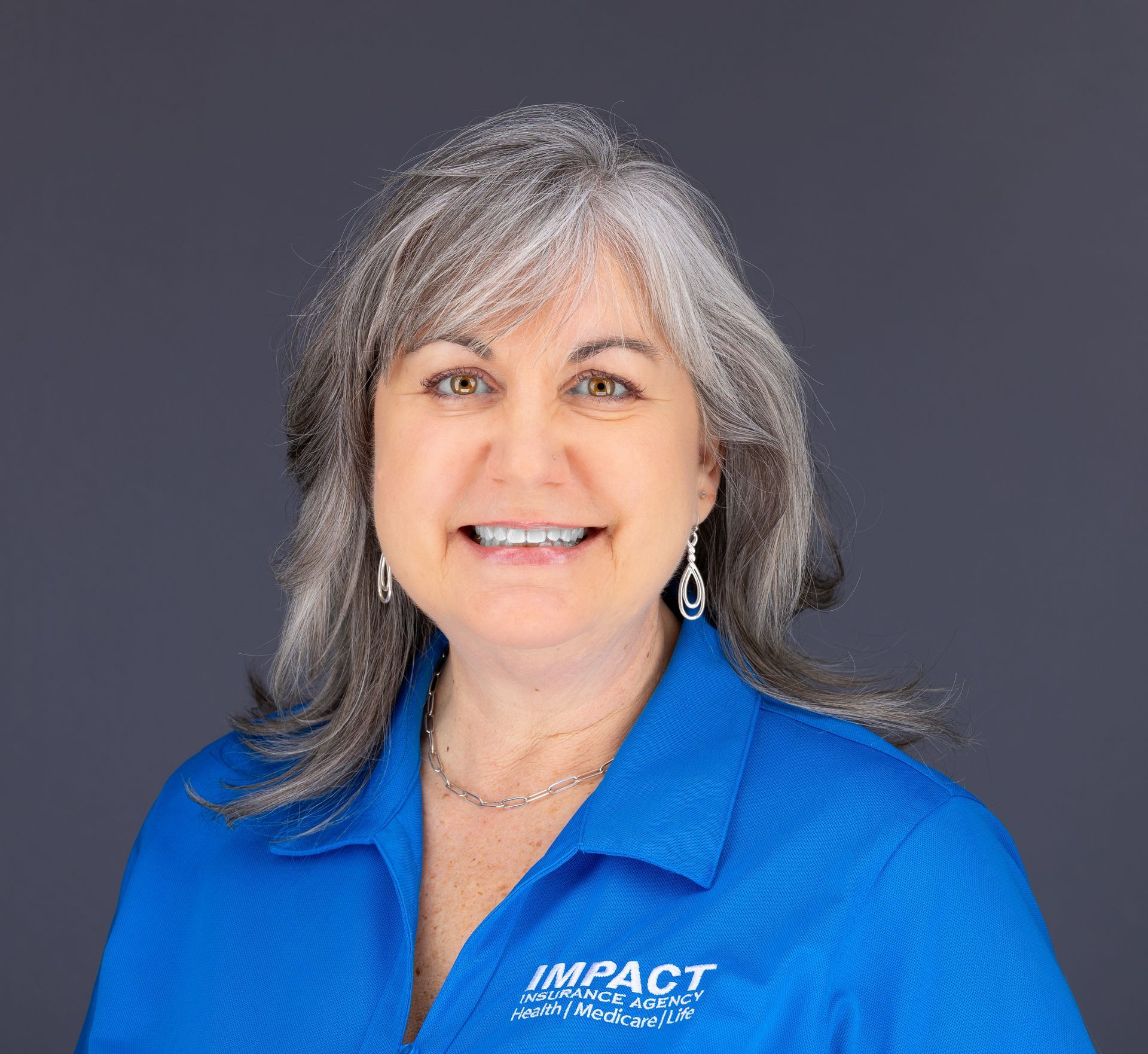 Woman with gray hair smiles, wearing a black top, against a light gray background.
