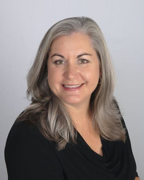 Woman with gray hair smiles, wearing a black top, against a light gray background.