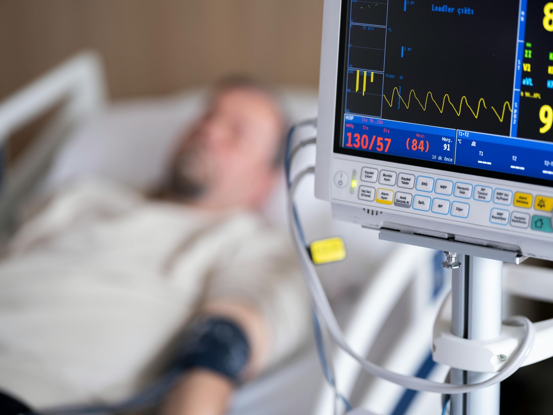 Man in hospital bed monitored by medical equipment.