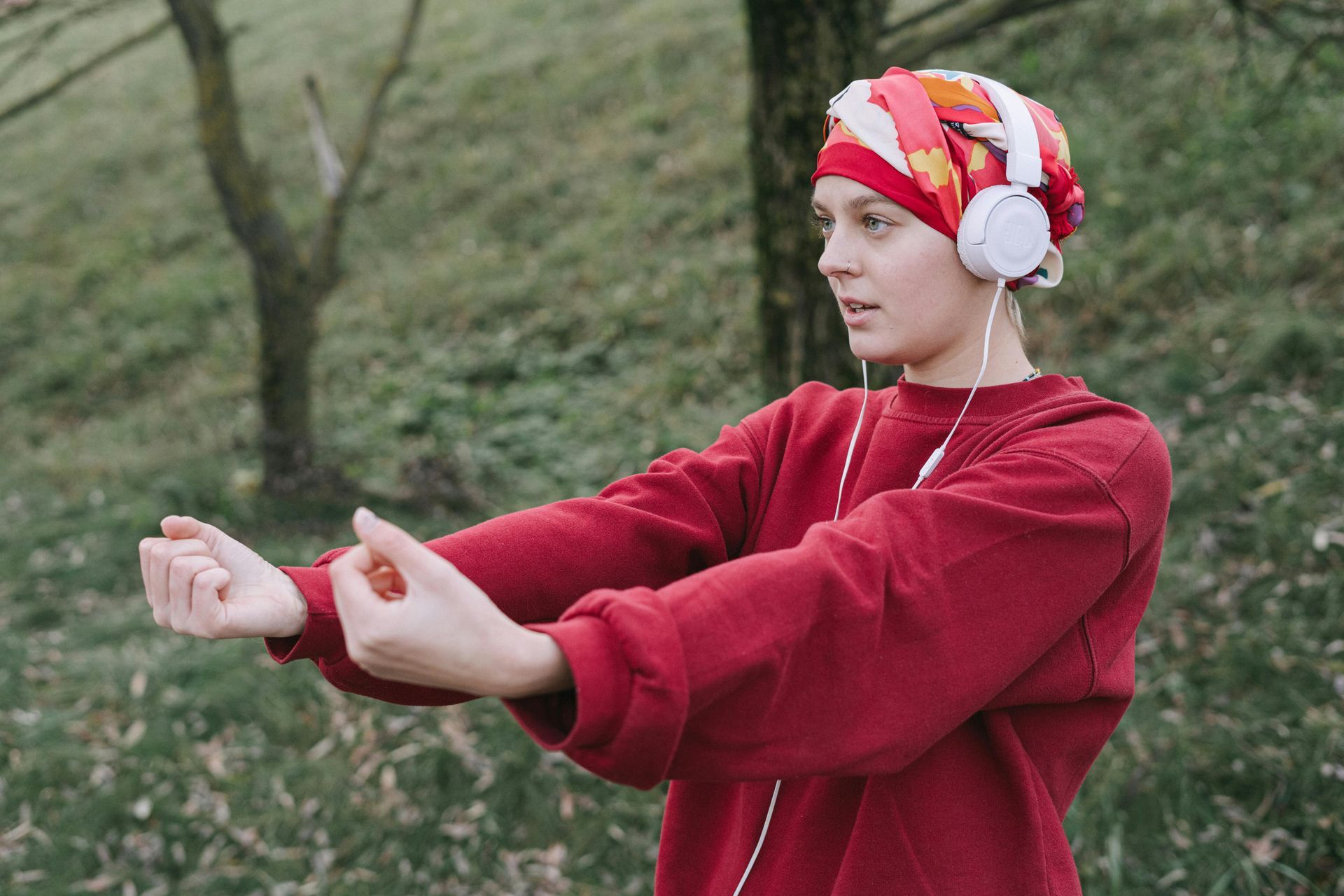Woman with headscarf and headphones practicing tai chi outdoors.