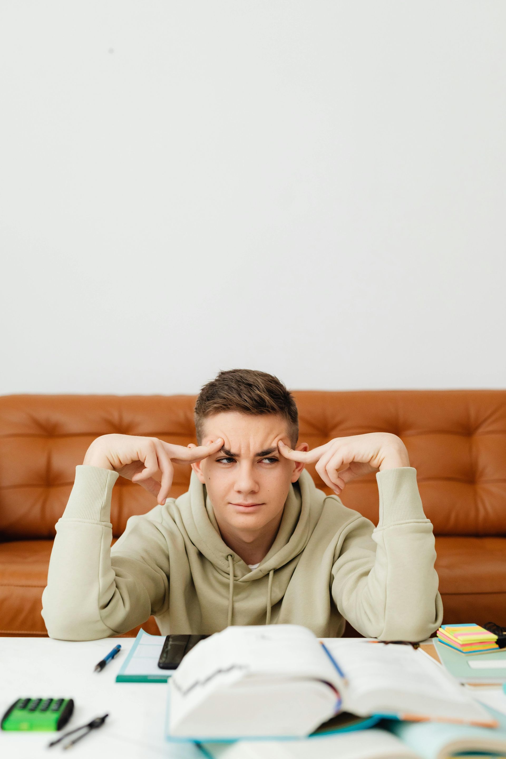 Teenager at desk, frowning, fingers to temples; books and calculator in front of him.
