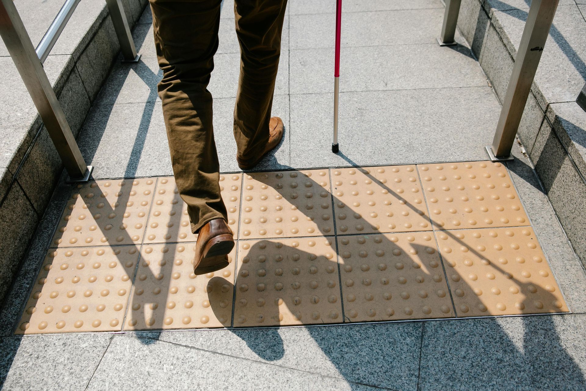 Person with cane walking on tactile paving at a subway entrance.