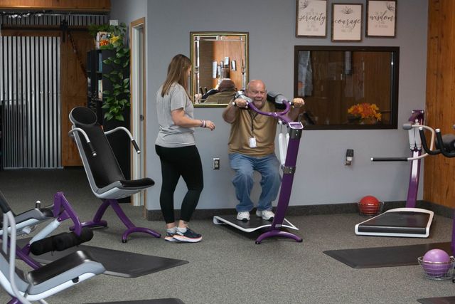 a man is sitting on a machine in a gym while a woman stands next to him