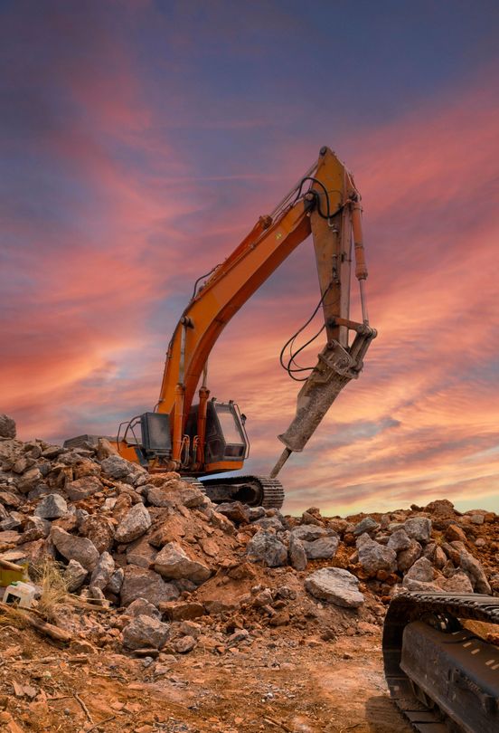 A bulldozer with torn up ground around it and pretty sunset in the sky behind it