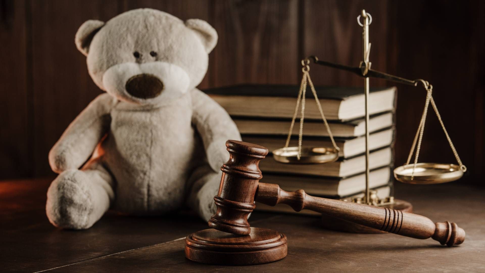 A teddy bear is sitting next to a judge 's gavel and scales of justice.