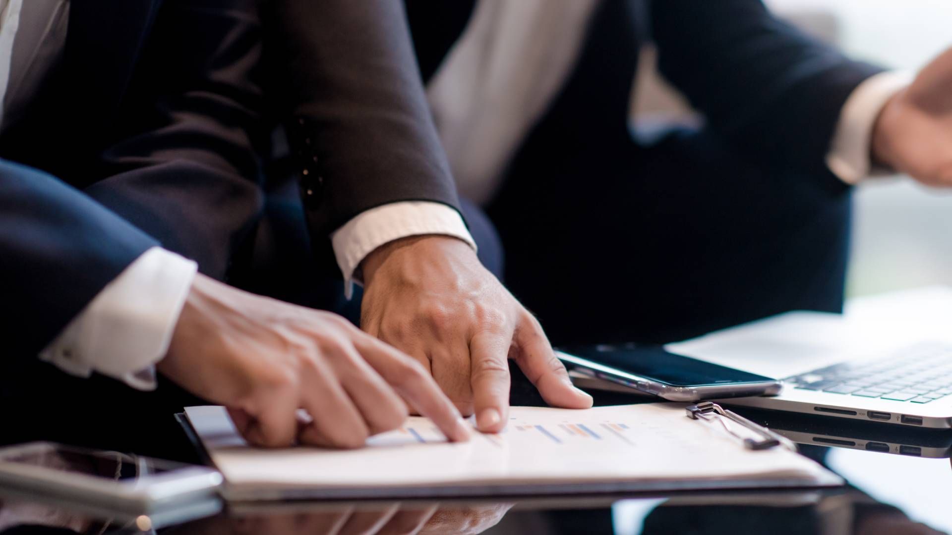 A group of business people are sitting at a table looking at a clipboard.