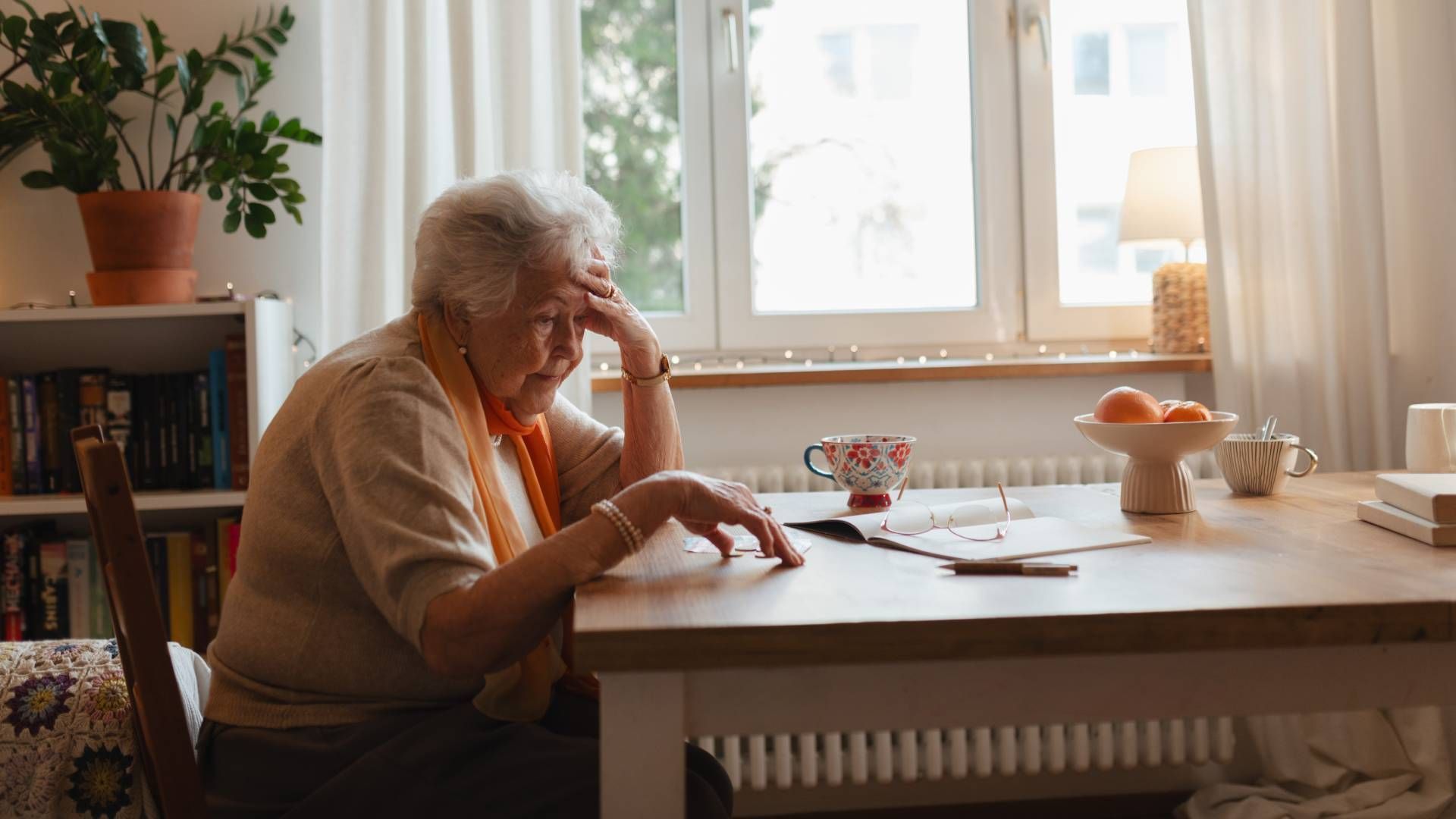 An elderly woman is sitting at a table in front of a window.