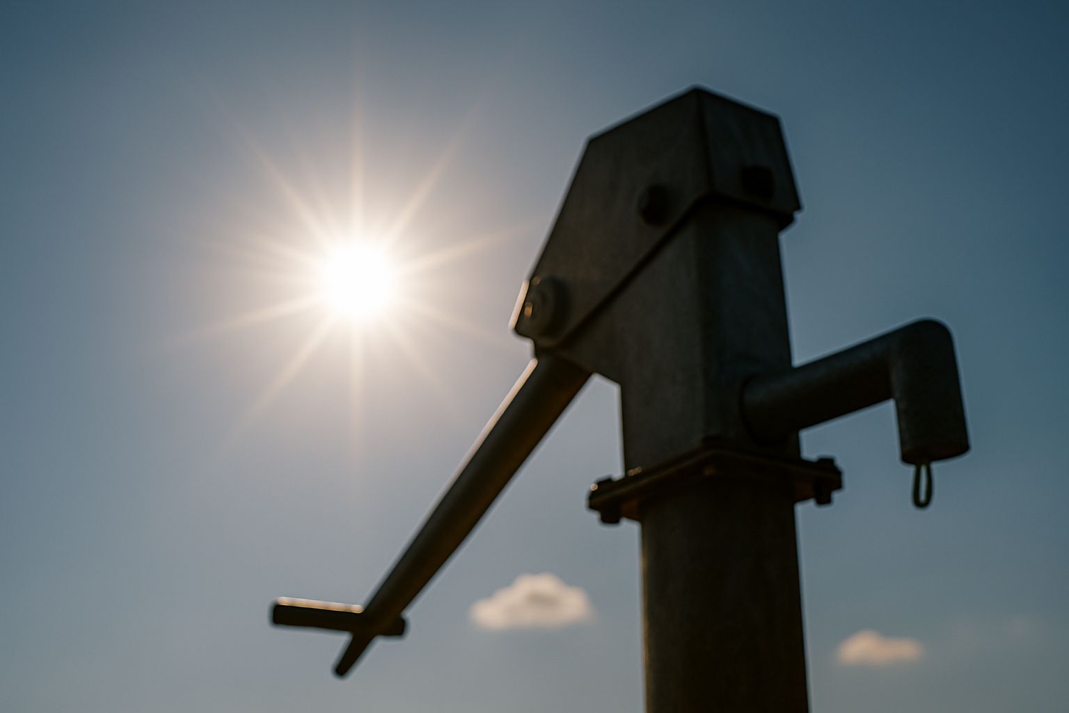 Hand water pump silhouetted against the sun in a blue sky.