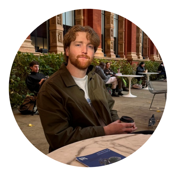A man with red hair and beard sits outside, holding a coffee cup. He wears a green jacket.