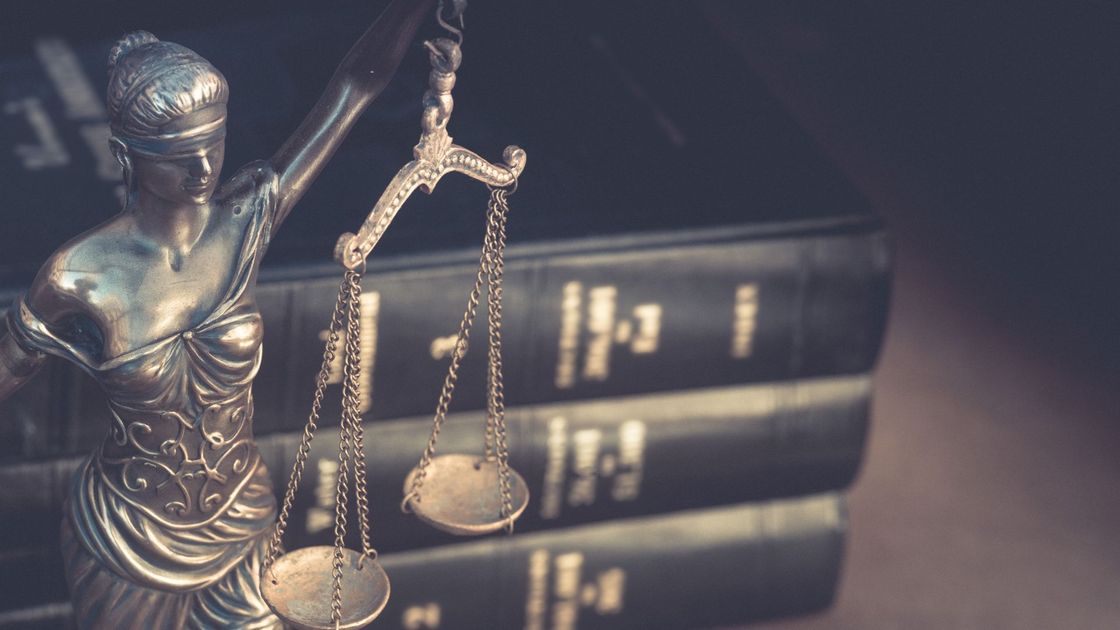 A statue of lady justice holding scales of justice in front of a stack of books.