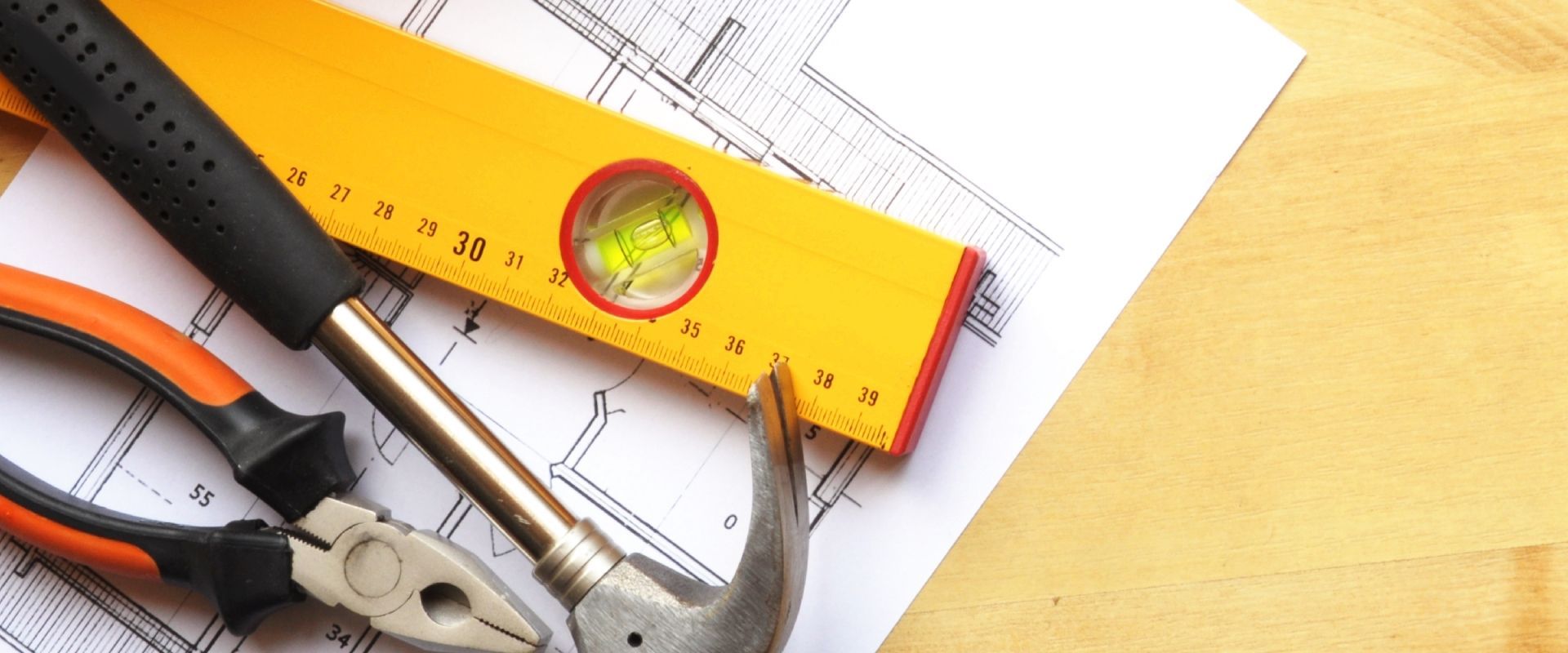 A pair of pliers , a hammer , and a level are sitting on top of a blueprint.